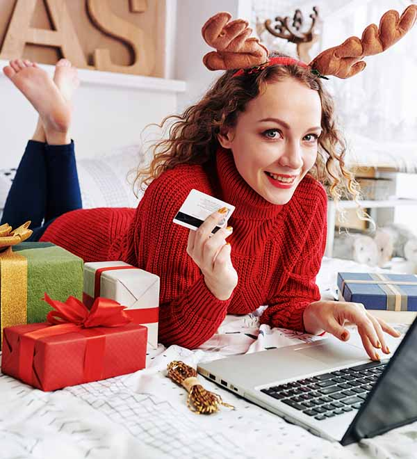Mujer compra regalos navideños con su tarjeta bancaria en un ordernador portátil
