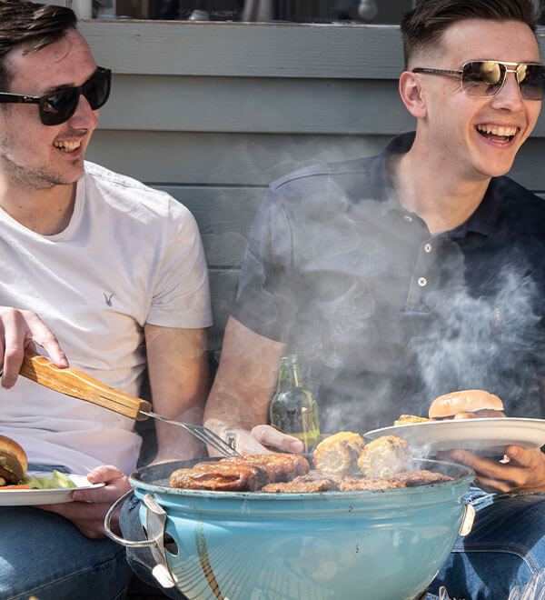 Twee mannen met een zonnebril op zitten naast een barbecue