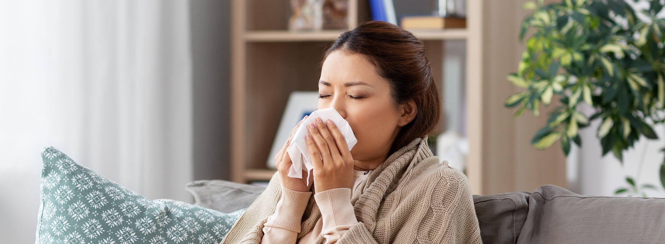 Woman sat on the sofa sneezing into a tissue