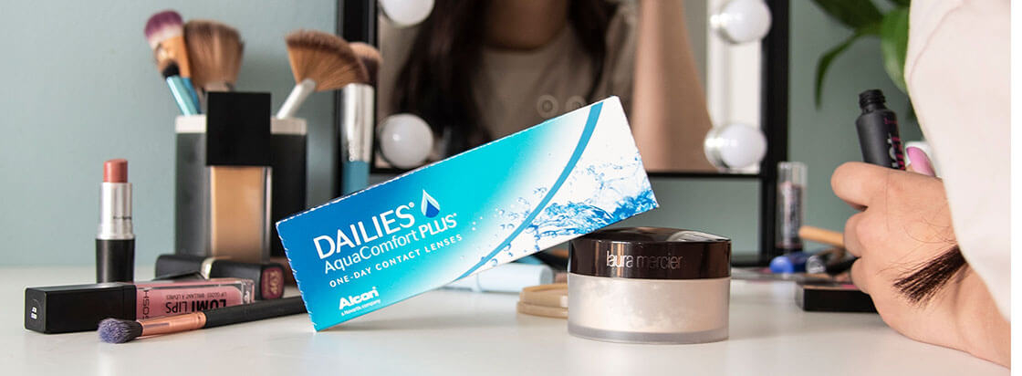 Produits de maquillage et boîte de lentilles de contact Dailies AquaComfort PLUS placés à côté d’une femme en train de se maquiller
