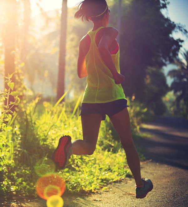 Een vrouw in een geel hemdje is aan het hardlopen in een groene omgeving