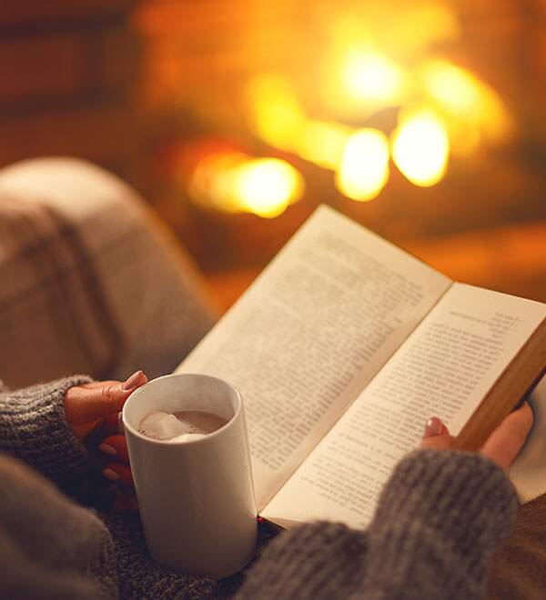 Woman reads book by the fire while holding a mug