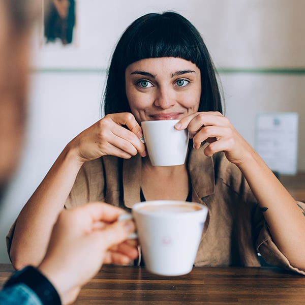 Een vrouw zit aan tafel en drinkt een kop koffie