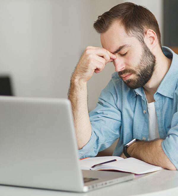 Een man werkt achter de laptop en wrijft in zijn ogen