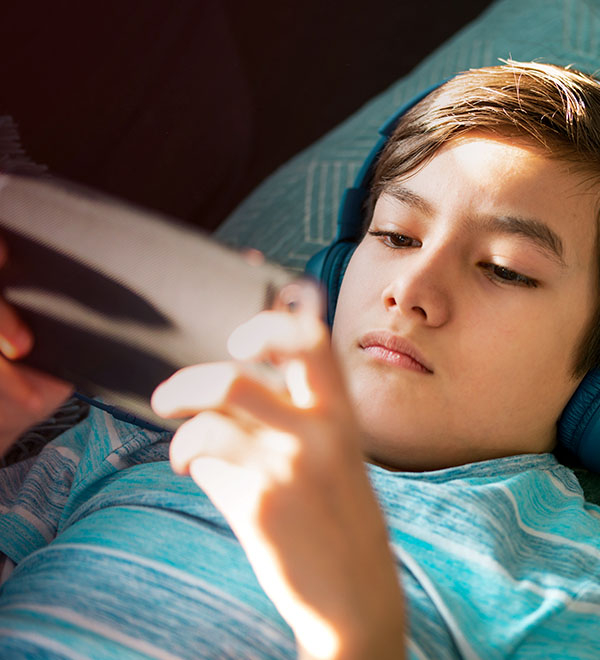 Een jongen met een koptelefoon op kijkt liggend naar een smartphone.